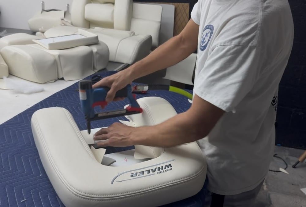 The craftsman fastens stainless steel staples to the captain's chair using an air gun.